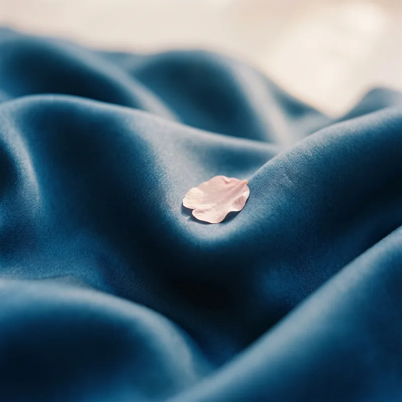 Deep blue silk fabric with a cherry blossom petal resting on it